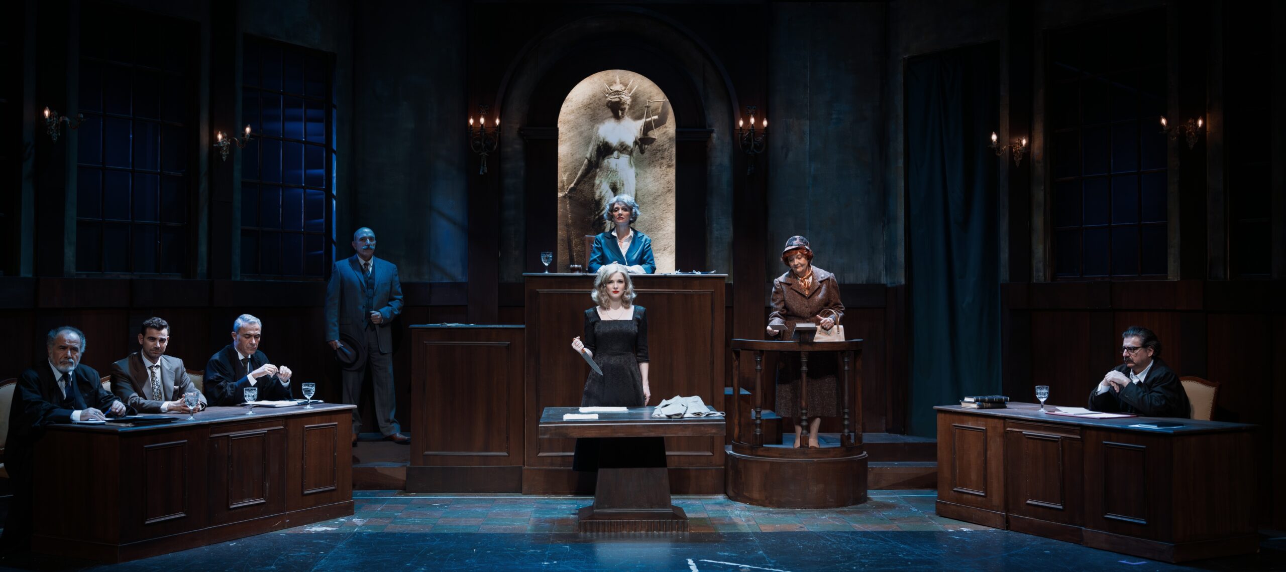 Μαθήματα φωτισμών Αίθουσα δικαστηρίου. Η δικαστής υπερυψωμένη, κάτω δεξιά και αριστερά της αίθουσας είναι τα τραπέζια όπου κάθονται οι συνήγοροι υπεράσπισης και κατηγορίας, ενώ στο κέντρο μια ξανθιά όμορφη γυναίκα στέκεται στο εδώλιο του κατηγορούμενου με το ένα χέρι στη μέση και κοιτάζει τον φακό.