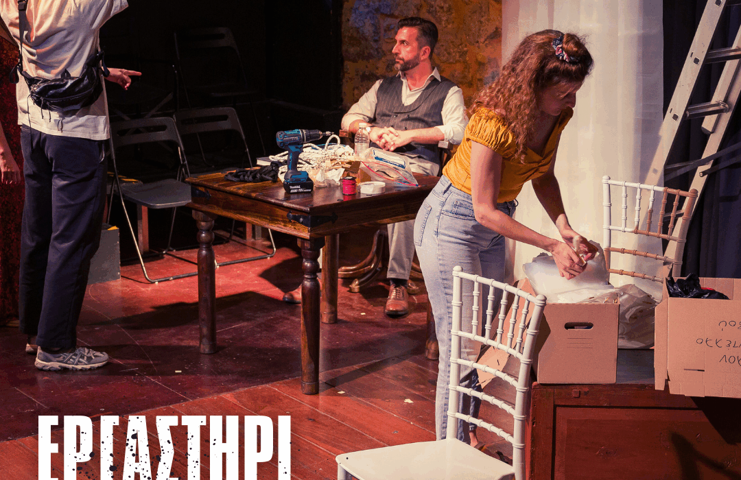 Σε θεατρική σκηνή κατά τη διάρκεια πρόβας, μια γυναίκα με κίτρινο μπλουζάκι και τζιν σκύβει πάνω από ένα ανοιχτό χαρτόκουτο, τακτοποιώντας υλικά. Δίπλα της υπάρχει λευκή καρέκλα και μια ξύλινη τράπεζα με εργαλεία, όπως ένα δράπανο και διάφορα μικροαντικείμενα. Πίσω της, ένας άντρας κάθεται στο τραπέζι κοιτώντας προς τα αριστερά, ενώ ακόμη δύο άτομα συζητούν εκτός κέντρου. Στο βάθος φαίνεται πέτρινος τοίχος, σκάλα και σκηνικός εξοπλισμός. Στο κάτω μέρος της εικόνας υπάρχει ο τίτλος “Εργαστήρι Σκηνογραφίας”