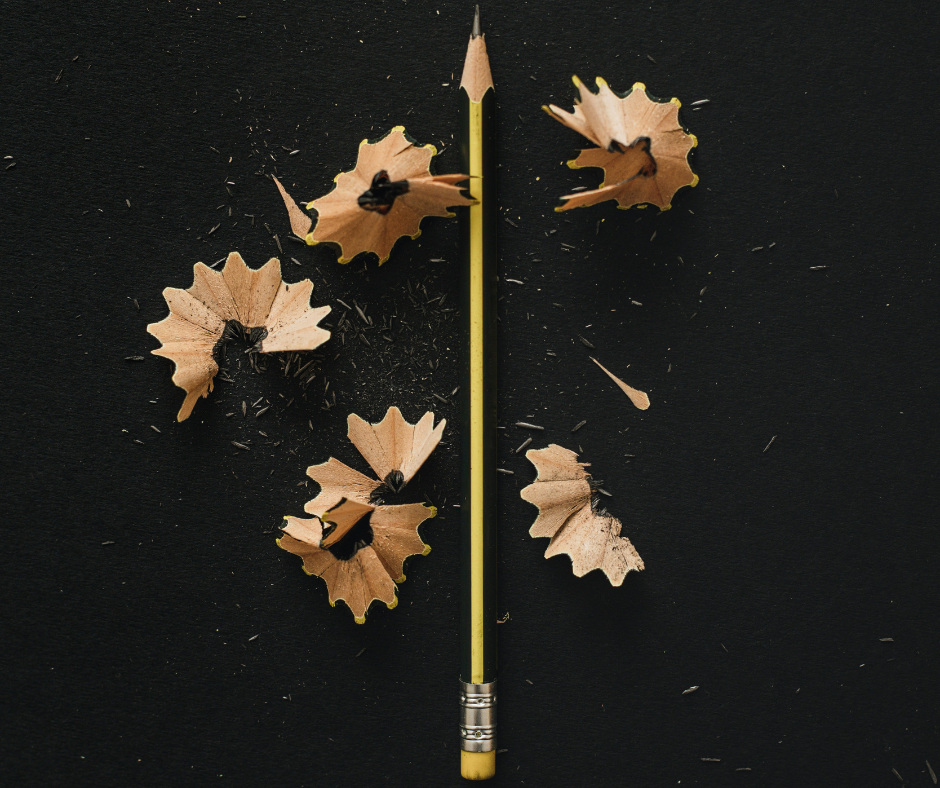 Ένα ξύλινο μολύβι σε μαύρο φόντο, πλαισιωμένο από ξύσματα που σχηματίζουν κύκλο γύρω του, συμβολίζοντας τη διαδικασία της δημιουργικής γραφής και της έμπνευσης που γεννιέται μέσα από τη δουλειά και την τεχνική.